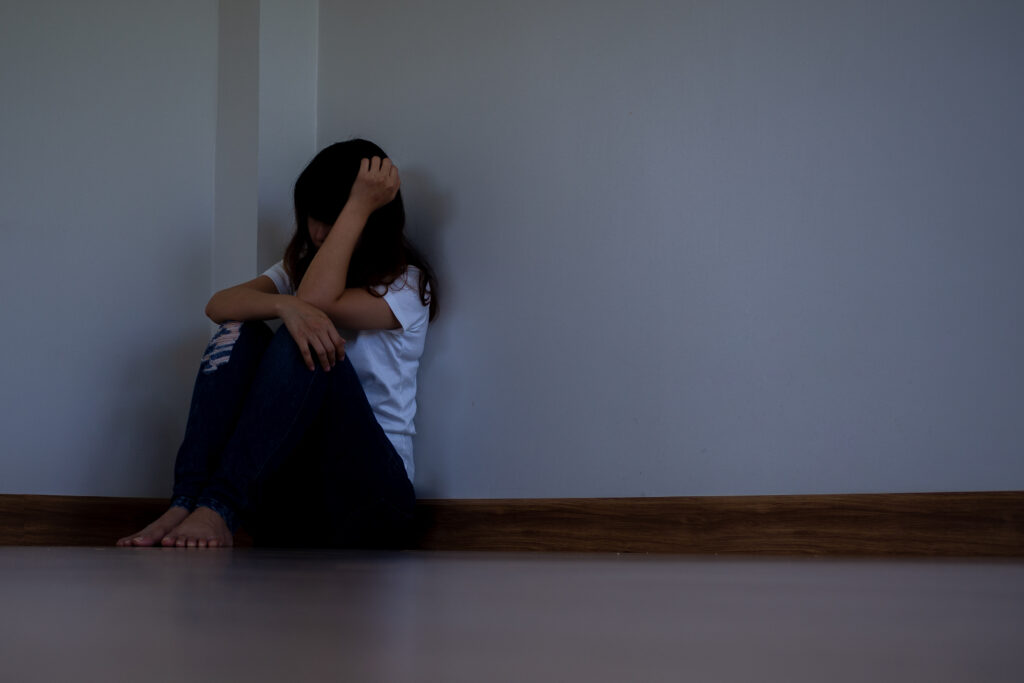 teen girl with self-esteem issues caused by acne sitting in a corner with hands across her face